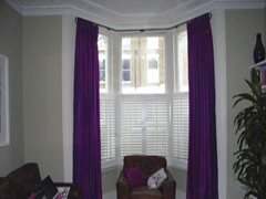Silk curtains with Pinch Pleat heading on bay window pole with cafe height shutters East London