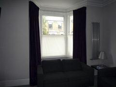 Velvet curtains, interlined and pinch-pleated, on corded steel bay window track together with simple bottom up blinds Tufnell Park