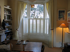 Simple lined linen curtains on bay rack with half-height shutters Islington